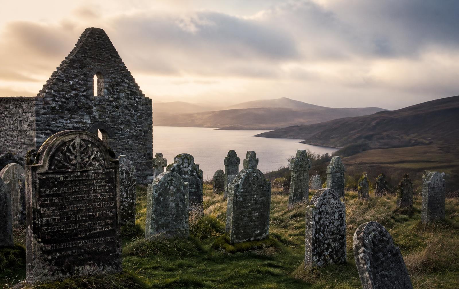 An ancient Scottish kirkyard of carved gravestones above a Highland loch at golden hour